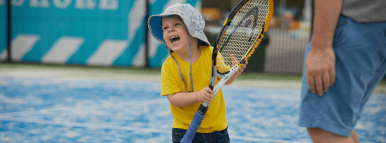 An excited child with an adult tennis racket
