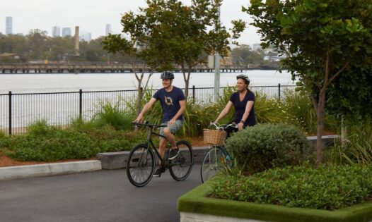 Two people riding bicycles on a path by a waterfront.