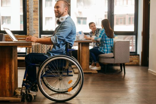 Man in a wheelchair working on a laptop in a cosy co-working space.