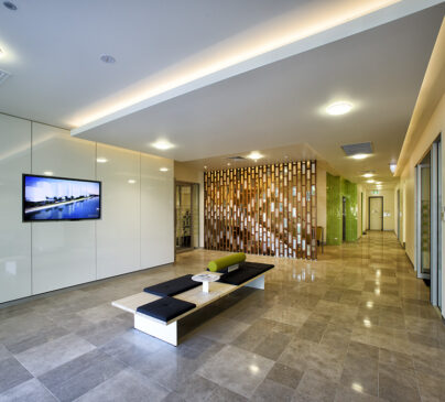 Modern office lobby at The Suites by Graystone with sleek white walls, a wall-mounted TV displaying a cityscape, and a decorative wooden wall feature.