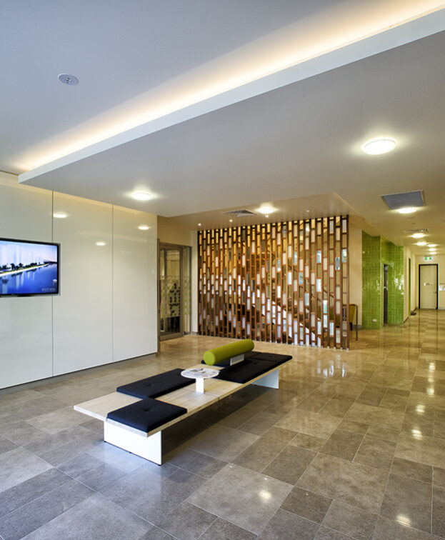 Modern office lobby at The Suites by Graystone with sleek white walls, a wall-mounted TV displaying a cityscape, and a decorative wooden wall feature.