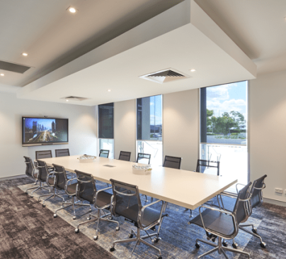A modern conference room with a long white table surrounded by ten black chairs at The Suites by Graystone.