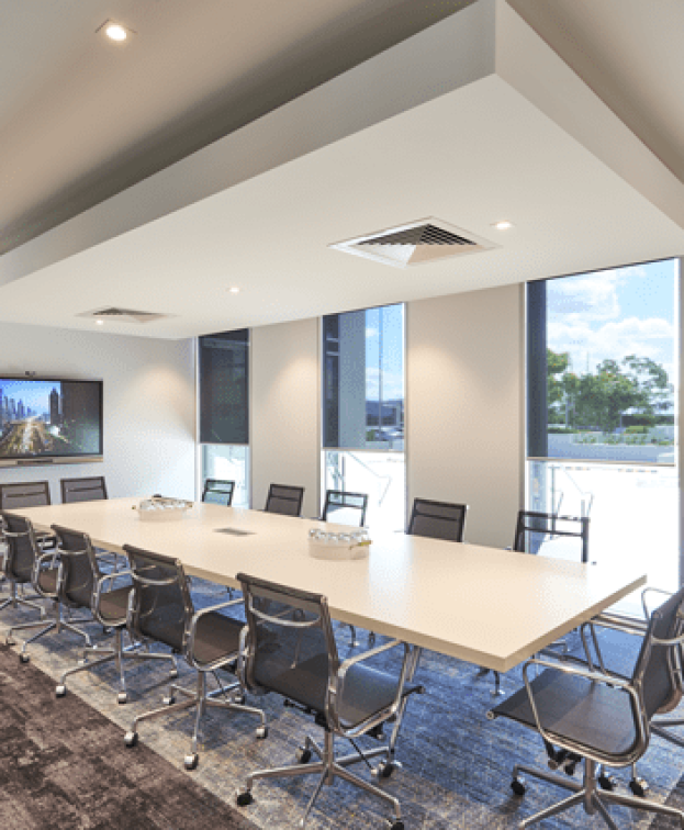A modern conference room with a long white table surrounded by ten black chairs at The Suites by Graystone.