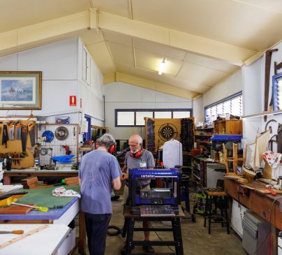 Men working in an interior workshop space surrounded by tools and timber.