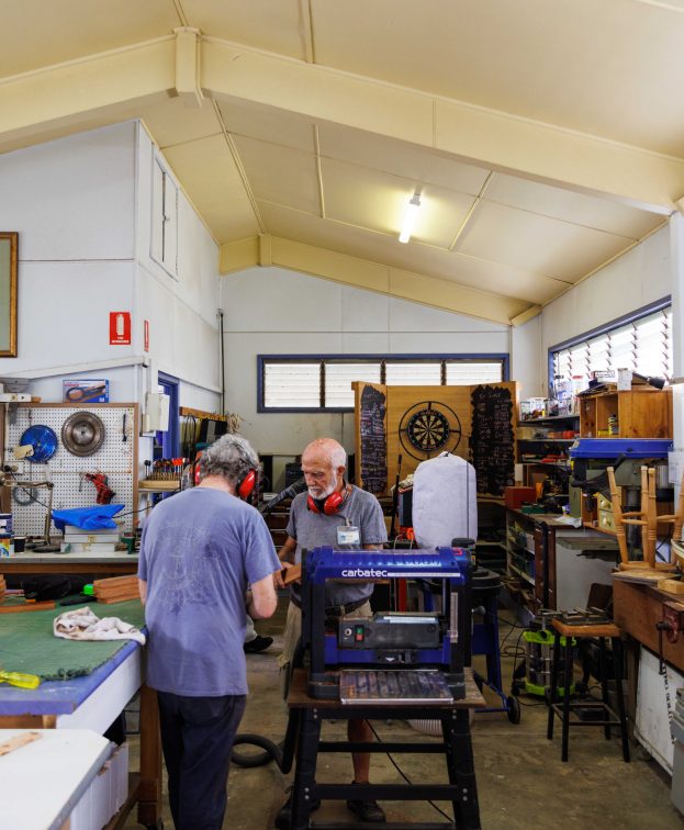Men working in an interior workshop space surrounded by tools and timber.