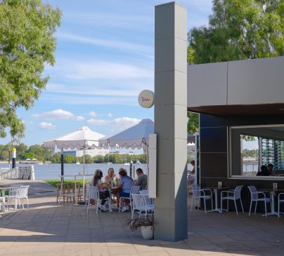 Outdoor dining at Riva, with several people sitting at tables under umbrellas near the Brisbane river.