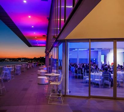 An elegantly lit venues with large windows reveals guests seated at tables during an event.