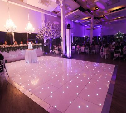 Waters Edge styled for a wedding reception with a glossy dance floor, elegant floral arrangements and sparkling lighting.