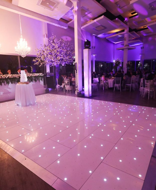 Waters Edge styled for a wedding reception with a glossy dance floor, elegant floral arrangements and sparkling lighting.