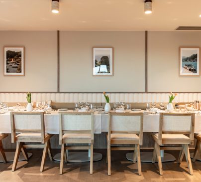 A long dining table at Riva is elegantly set with white tablecloth, numerous place settings, and flowers.