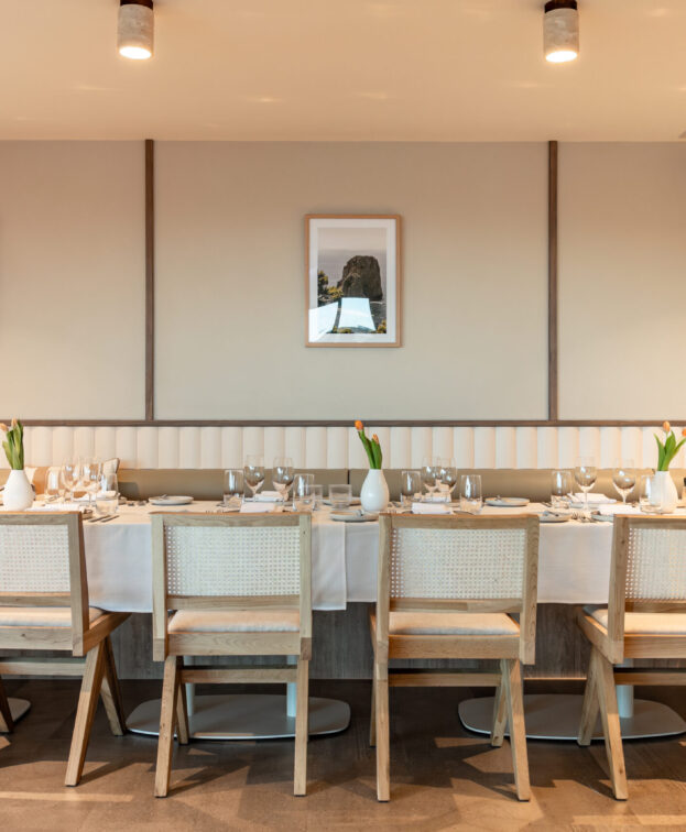 A long dining table at Riva is elegantly set with white tablecloth, numerous place settings, and flowers.