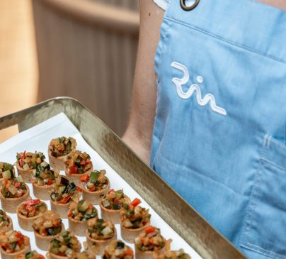 A person in a light blue Riva apron holds a tray of appetizers.