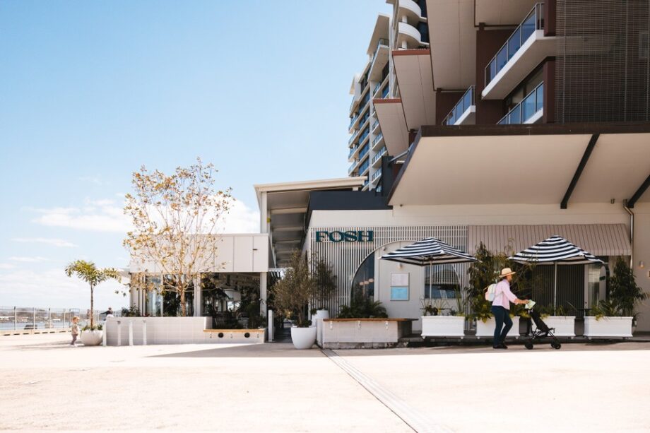 Aa modern building with a sign that reads FOSH. The building has striped umbrellas and outdoor seating.