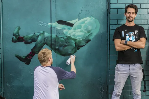 Lincoln Savage, Creative Director, standing with folded arms, smiling, next to an artist painting a mural.